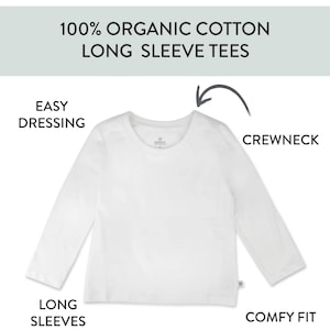 Op de afbeelding: Een wit shirt met lange mouwen en een ronde hals, gemaakt van 100% biologisch katoen. De afbeelding bevat de teksten: 100% ORGANIC COTTON LONG SLEEVE TEES, EASY DRESSING, CREWNECK, LONG SLEEVES en COMFY FIT, met een pijl naar de halslijn.