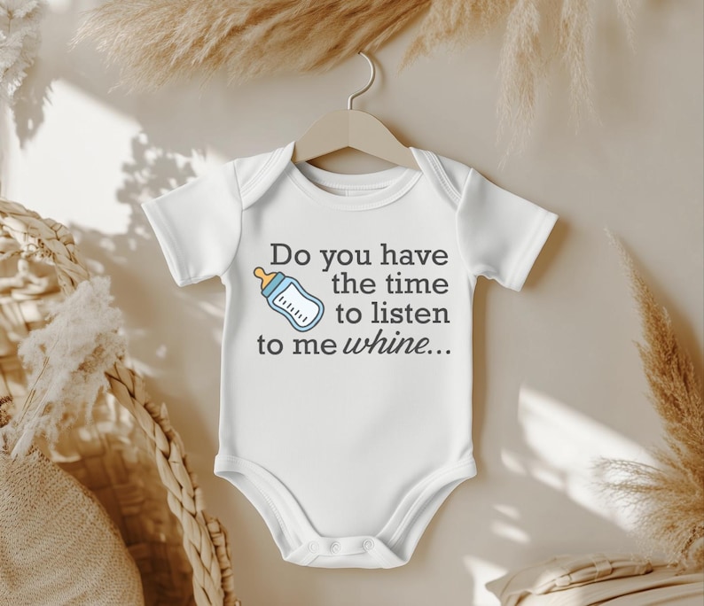 May include: White baby onesie with the text "Do you have the time to listen to me whine..." and a cartoon bottle graphic. The onesie is hanging on a wooden hanger against a neutral background.