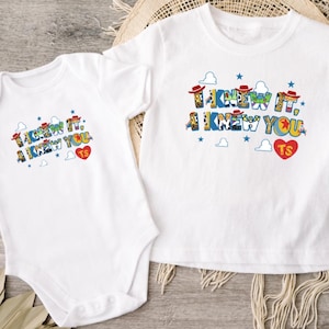 Puede incluir: Un body de beb&eacute; blanco de manga corta y una camiseta blanca de manga corta. Ambas prendas presentan un estampado gr&aacute;fico colorido con el texto "I KNEW IT, I KNEW YOU" en una fuente estilizada, acompa&ntilde;ado de peque&ntilde;as estrellas azules, nubes y un coraz&oacute;n rojo con "TS".