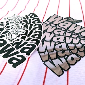 May include: Two stacks of stickers with the word "Wawa" in a bold font. One stack features a black and white bird graphic, while the other has a silver metallic finish. The stickers are on a white fabric with red stripes.