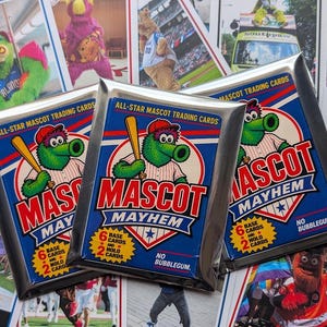 Op de afbeelding: Drie verzegelde folieverpakkingen met Mascot Mayhem-verzamelkaarten met een groen mascottefiguur dat een honkbalknuppel vasthoudt. Elke verpakking toont de tekst All-Star Mascot Trading Cards, Mascot Mayhem, 6 base cards en 2 holo cards.