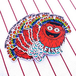Könnte beinhalten: Ein Stapel Aufkleber mit einem roten Cartoon-Monster und dem Text "EQUAL RIGHTS" in Regenbogenfarben. Die Aufkleber zeigen auch "GRITTY SAYS" und "OR ELSE!" auf einem weiß-rot gestreiften Hintergrund.