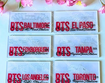 May include: Rectangular clear glass coasters with red text that reads "BTS" followed by a city name and stadium name. The coasters feature a stadium architectural drawing. Cities include Baltimore, El Paso, Foxborough, Tampa, Los Angeles, and Toronto.