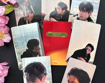 May include: A selection of photo cards displaying a person in different poses. The cards are rectangular with images on the front. A red booklet with gold text is also present. Pink flowers are in the background.