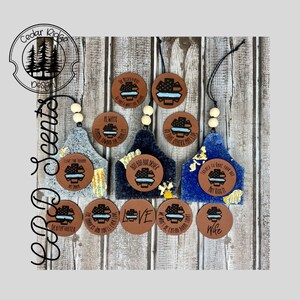 May include: A set of nine brown leather car air fresheners with blue and white thin blue line designs. The air fresheners have various sayings on them, including "Boo Boo Bus Driver", "Trained to Have Your Back Not Kiss It", "The Hardest Job You'll Ever Love", "Wife", "We Won't Be Eating Mom Tonight", "Love", "Deathfighter", "Live One From Another", and "Always Aiming Downward For The Target".