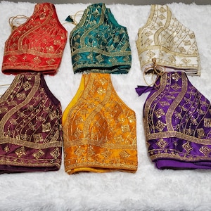 May include: Six embroidered fabric choli tops in various colors, including red, green, white, purple, gold, and brown. Each top features a geometric pattern with gold embellishments.