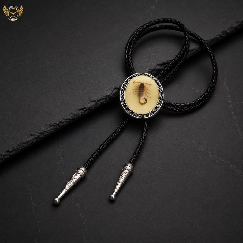 Pu&ograve; includere: Una cravatta a bolo nera con un ciondolo circolare raffigurante uno scorpione in resina trasparente. Il ciondolo &egrave; incorniciato da un bordo color argento. La cravatta ha un cordino nero intrecciato con punte color argento.