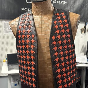 Puede incluir: Un chaleco de cuero negro con un patrón de pata de gallo rojo y negro. El chaleco está en un maniquí.