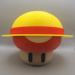 May include: A 3D printed mushroom figurine with a yellow and red hat. The mushroom is brown with black eyes.