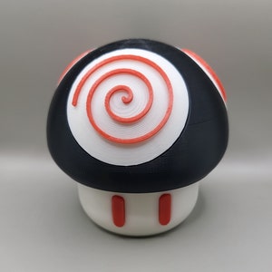 May include: A black and white mushroom-shaped object with a red spiral design on the top. The mushroom has a white stem with two red stripes.