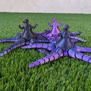 May include: Three purple and black octopus figurines with human-like torsos and arms. The octopus figurines are posed with their arms outstretched. The figurines are on a green artificial grass surface.