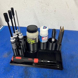 May include: A black organizer tray with various tools and accessories. It includes screwdrivers, bottles, a small flashlight, and other components. The tray is on a blue surface, and the tools are neatly arranged for easy access.