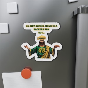 May include: A refrigerator magnet featuring a humorous image of Jesus wearing a Green Bay Packers jersey and a cheesehead. The text reads "I'm not saying Jesus is a Packers fan but..." and "Cheezus". The magnet has a white border.