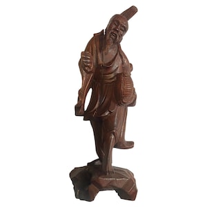 Peut inclure: Sculpture en bois détaillée d'un vieil homme en tenue traditionnelle. La figurine est représentée avec une longue barbe, tenant un panier et debout sur une base sculptée. Le bois est d'une riche couleur brun foncé, et la sculpture présente des détails complexes.