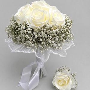 Könnte beinhalten: Ein Brautstrauß mit elfenbeinfarbenen Rosen und weißem Schleierkraut. Der Strauß ist mit weißer Spitze und Perlentrimm umwickelt und mit einem Satinband gebunden. Eine passende Ansteckblume mit einer einzelnen Rose ist ebenfalls enthalten.
