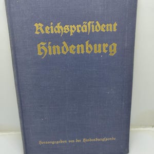 May include: A blue book with gold lettering that reads "Reichspräsident Hindenburg." The text "Herausgegeben von der Hindenburgspende" is printed at the bottom. The book has a textured cover.