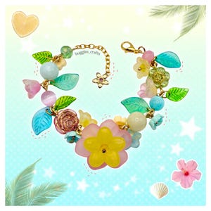 Pode incluir: Uma pulseira floral colorida com corrente e fecho dourados. A pulseira apresenta flores, contas e folhas rosa, amarelas, azuis e verdes. O texto "buggies_crafts" é visível na corrente.