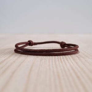 May include: A brown cord bracelet with a simple knot design.