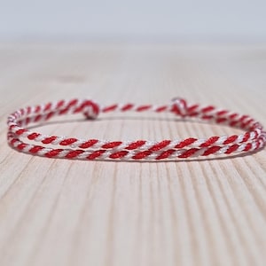 Könnte beinhalten: Ein rot-weißes geflochtenes Freundschaftsarmband. Das Armband besteht aus zwei Schnüren, einer roten und einer weißen, die miteinander geflochten sind.