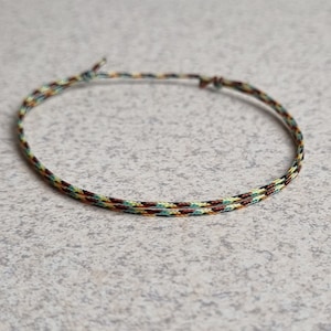 May include: A thin, braided bracelet with brown, yellow, and green threads.