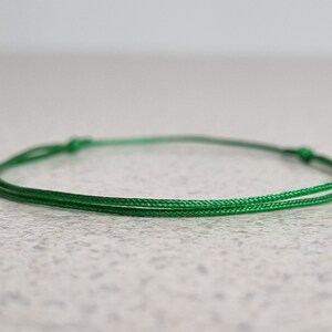 May include: A simple green string bracelet with a knotted closure.