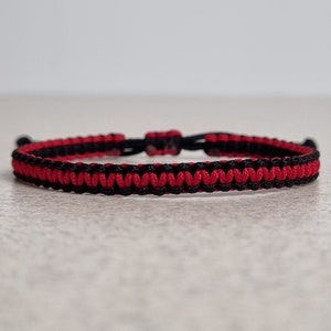 May include: A red and black braided bracelet with a knotted closure.