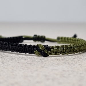 Op de afbeelding: Een gevlochten vriendschapsarmband in zwart en groen met een knoop in het midden.