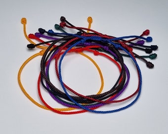 Può includere: Una collezione di braccialetti intrecciati colorati in rosso, arancione, giallo, verde, blu, viola e nero.