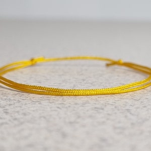 May include: A simple yellow string bracelet, tied in a knot.