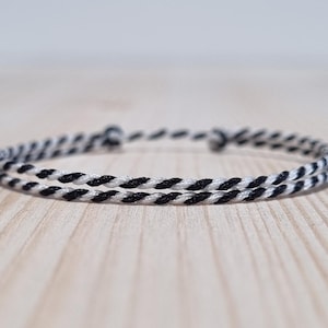 May include: A black and white braided bracelet. The bracelet is made of two strands of cord, one black and one white, that are twisted together.