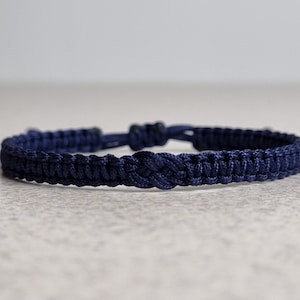 May include: A navy blue braided bracelet with a simple knot closure.