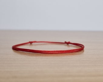 May include: A simple red string bracelet, tied with a knot at each end.