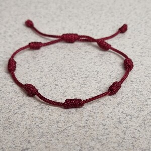 Op de afbeelding: Een geknoopte armband in bordeauxrood met meerdere knopen langs de armband.