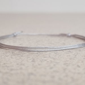 May include: A simple silver bracelet made of two strands of cord.