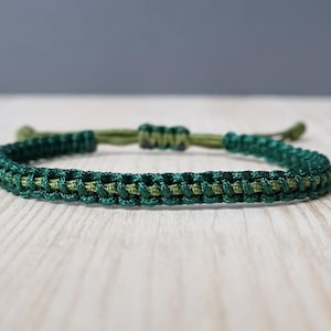 May include: A green and dark green braided bracelet with a knotted closure.