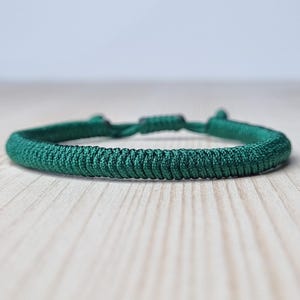 Könnte beinhalten: Ein geflochtenes Armband in Dunkelgrün.