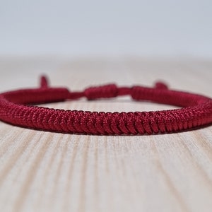 May include: A red braided cord bracelet with a knotted closure.