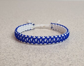 Op de afbeelding: Een blauw en wit gevlochten vriendschapsarmband. De armband is gemaakt met een eenvoudig knoopmotief.