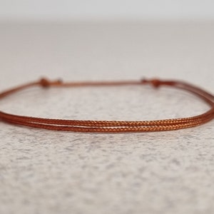 Può includere: Un semplice braccialetto in corda marrone con un design a doppio filo.