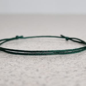 May include: A simple dark green cord bracelet with a knotted closure.