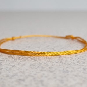 May include: A simple gold cord bracelet with a knotted closure.