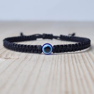May include: A black string bracelet with a blue evil eye charm. The bracelet is tied with a knot and is adjustable.