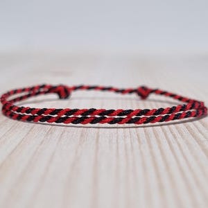 May include: A red and black braided bracelet. The bracelet is made of two strands of cord, one red and one black, that are braided together.