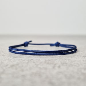 May include: A simple navy blue bracelet made of two strands of cord, tied with a knot at each end.