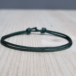 May include: A dark green cord bracelet with a simple knot closure.