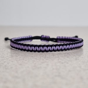 May include: A black and lavender braided bracelet with a simple knot closure.