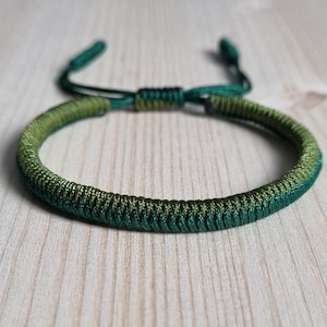 Pode incluir: Um bracelete trançado verde e verde escuro com fecho de nó.