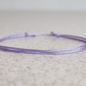 May include: A simple, delicate bracelet made of two strands of light purple cord.