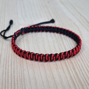 Puede incluir: Un brazalete trenzado negro y rojo con un cierre simple de nudo.