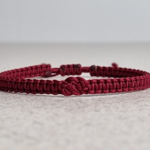 Puede incluir: Un brazalete trenzado rojo con un diseño de nudo.